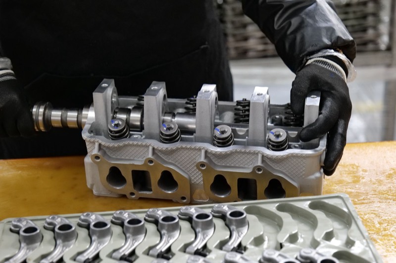 Gloved hands working on a cylinder head with the valve springs exposed.