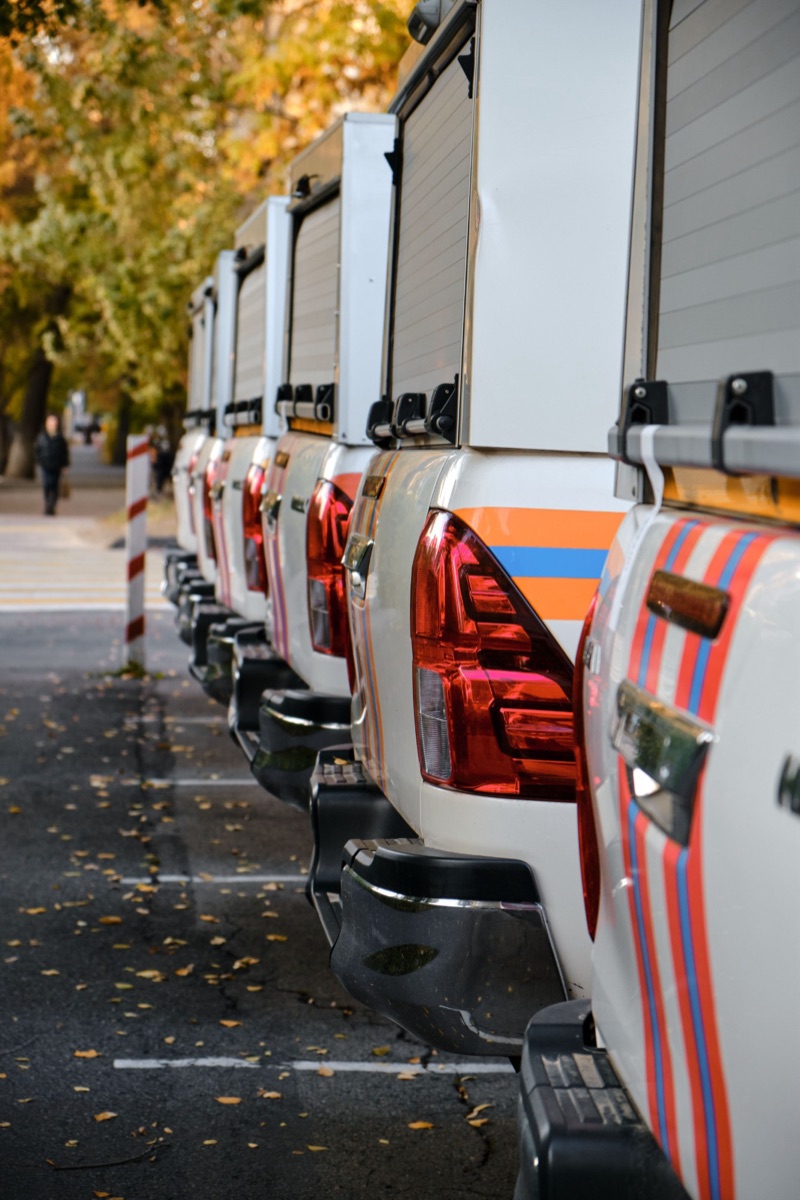 A row of white service-body work trucks parked along a street.