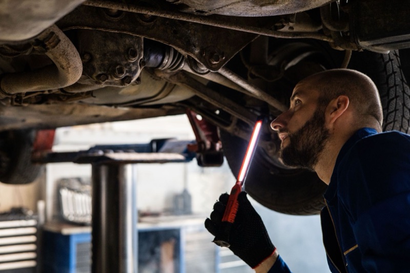 Mechanic inspecting the underside of a truck on a lift with a work light.