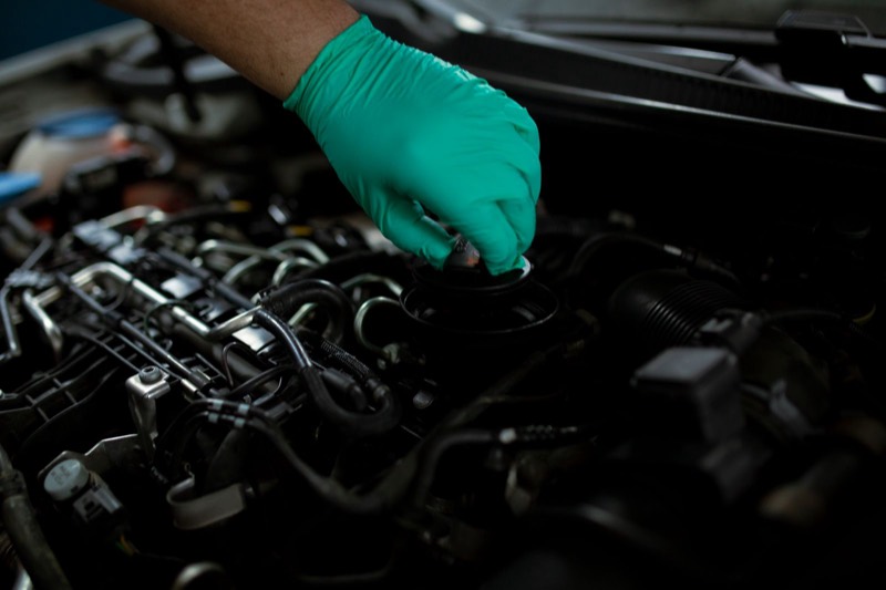 Gloved hand opening an engine oil filler cap.
